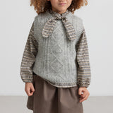 Pige iført grå strikvest over kjole og strømpebukser