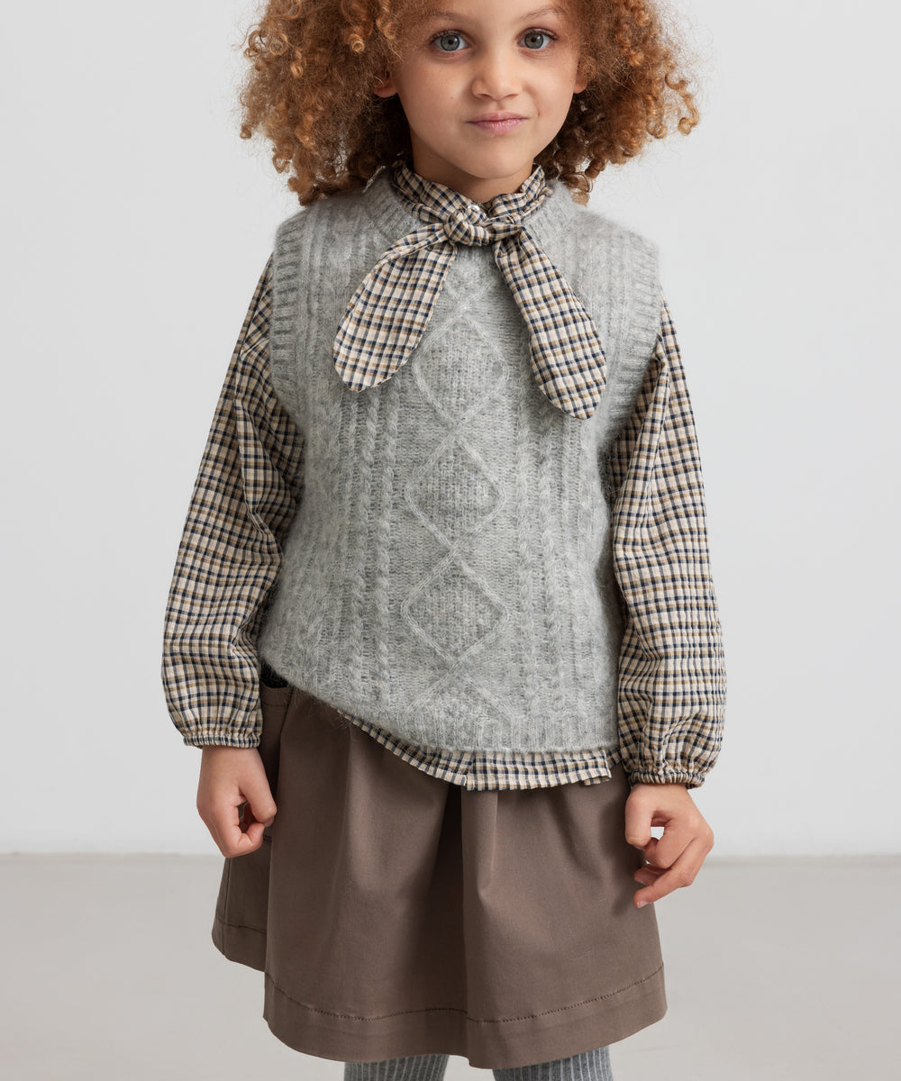 Pige iført brun ternet bluse under grå strikvest