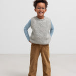 Dreng iført grå strikvest og brune bukser