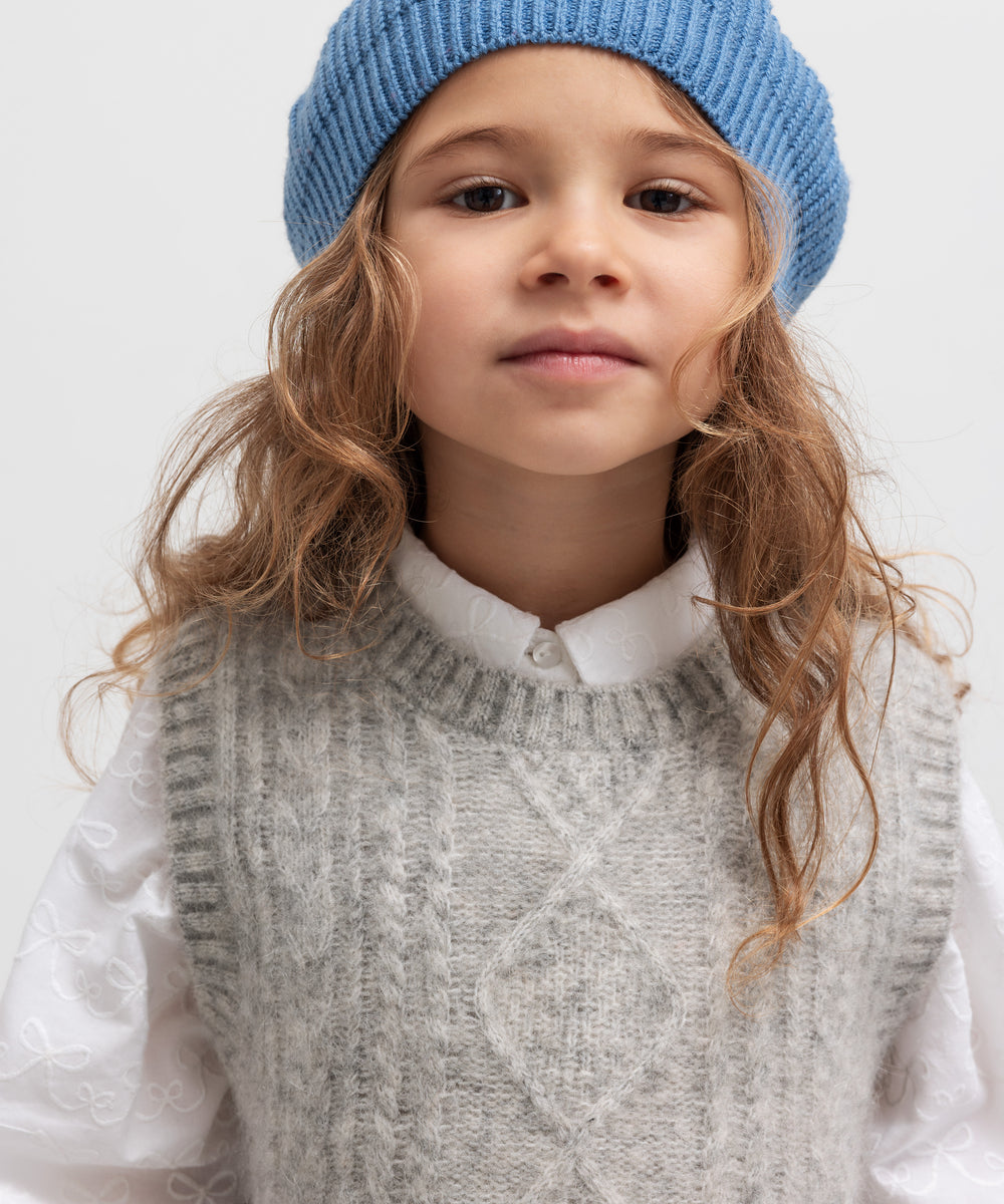 Pige med blå beret og rød kvast iført grå vest og hvid skjorte