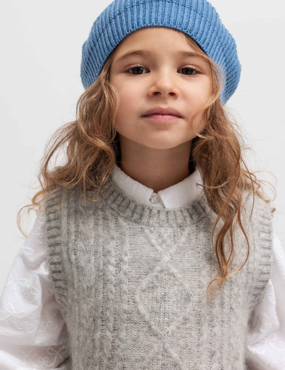 Pige med blå beret og rød kvast iført grå vest og hvid skjorte