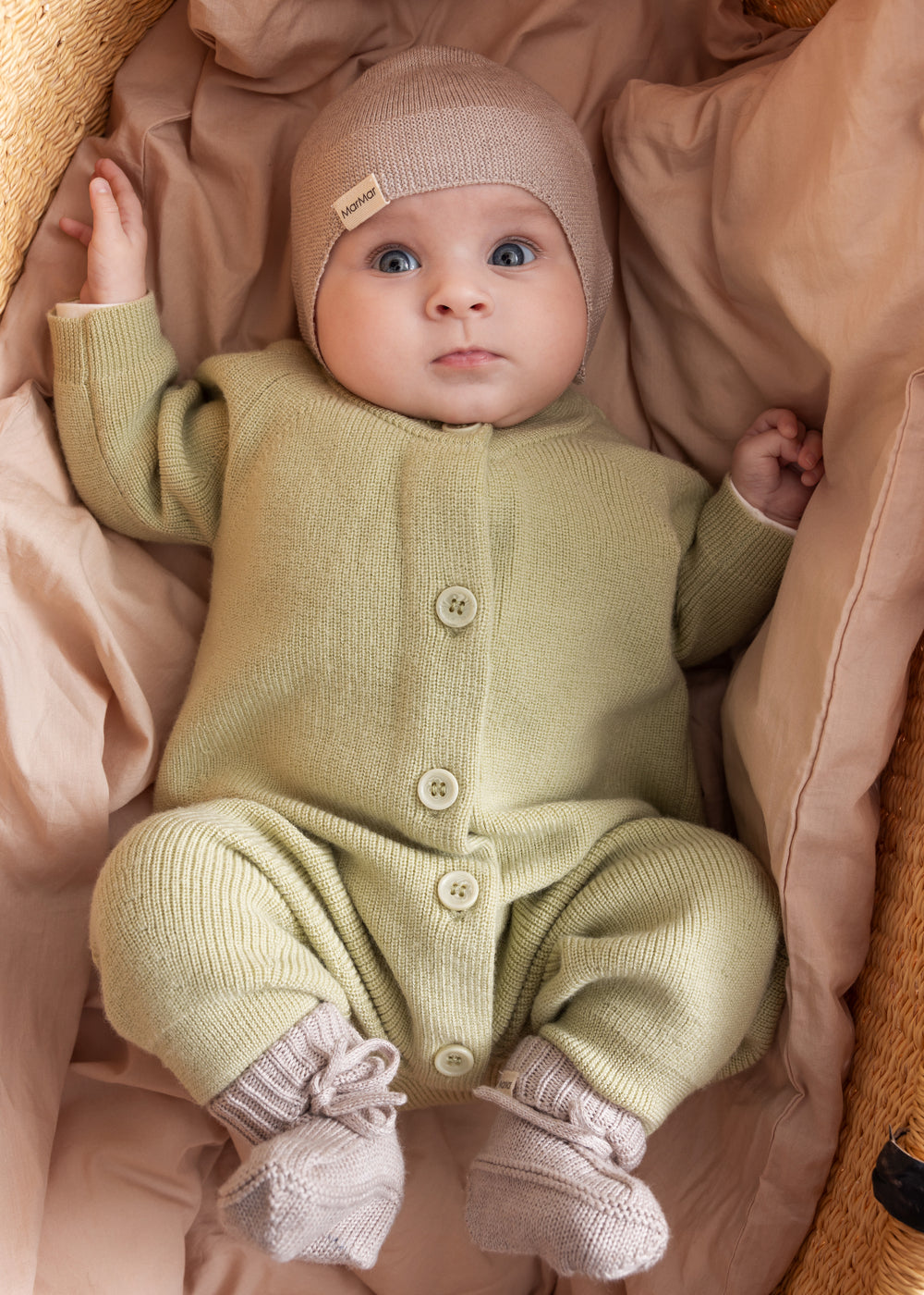 Baby iført blødt beige strikket heldragt med knapper foran