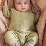 Baby iført blødt beige strikket heldragt med knapper foran