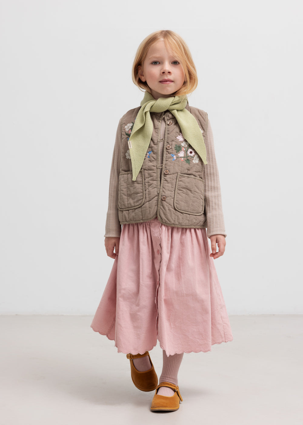 Pige iført beige quiltet vest med lommer og lyserød nederdel