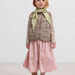 Pige iført beige quiltet vest med lommer og lyserød nederdel