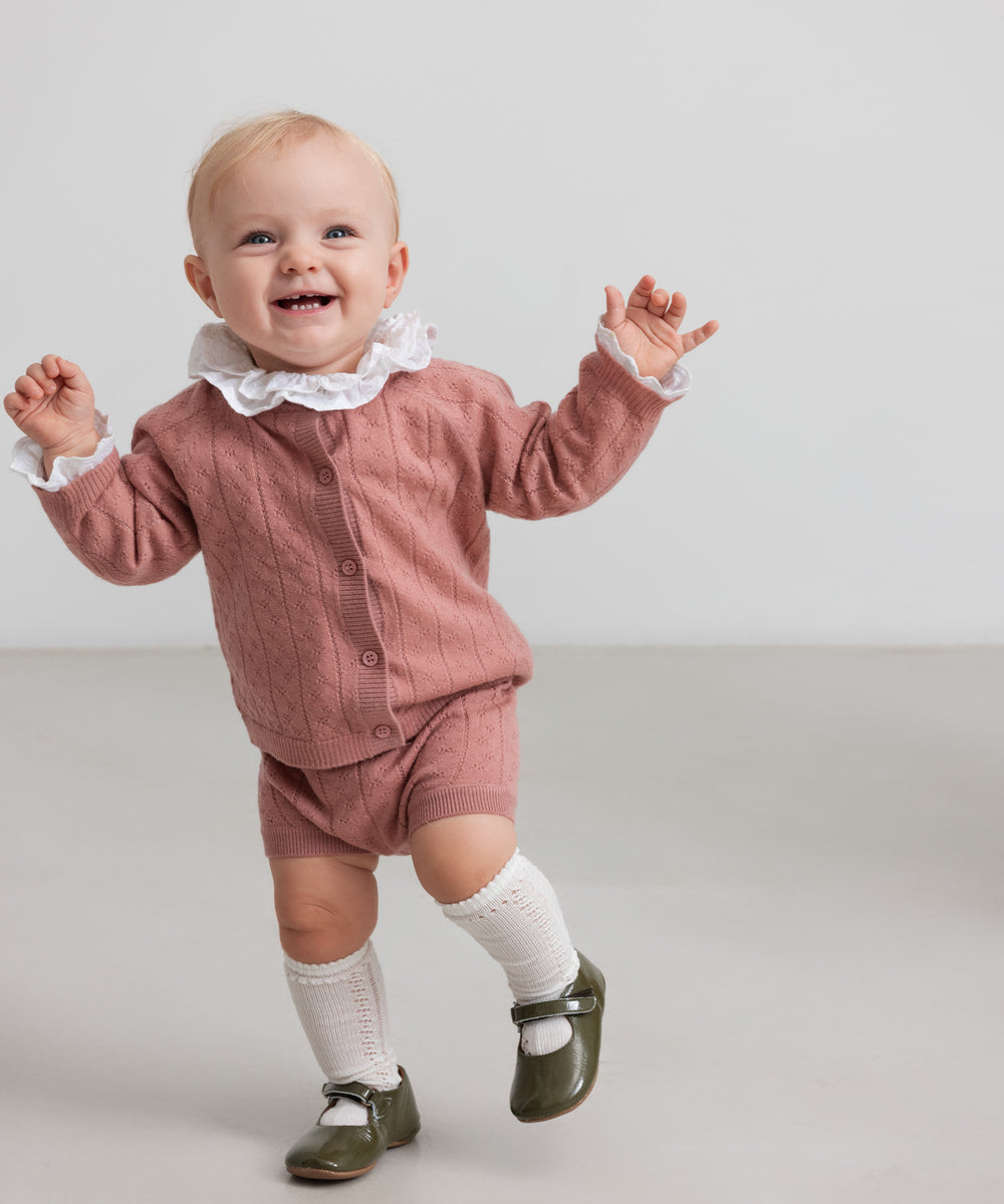 baby iført rosa strikket sæt med hvid flæsekrave