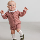 baby iført rosa strikket sæt med hvid flæsekrave