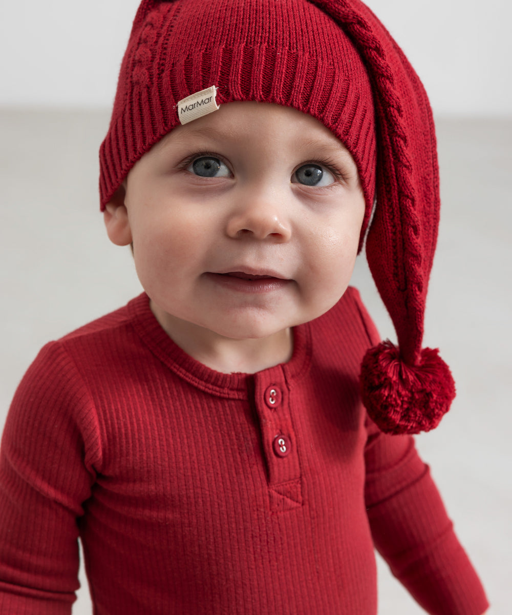 Baby iført rød ribbet body med stolpeknapper og nissehue
