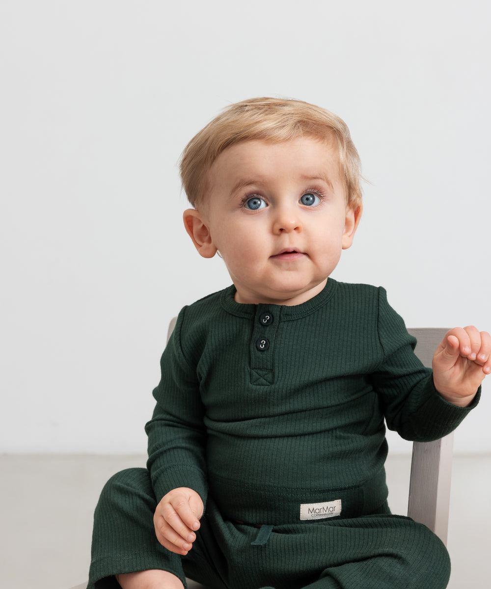 Baby iført mørkegrøn ribbet body med stolpeknapper