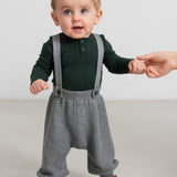 Baby iført mørkegrøn body og grå strikkede bukser med seler