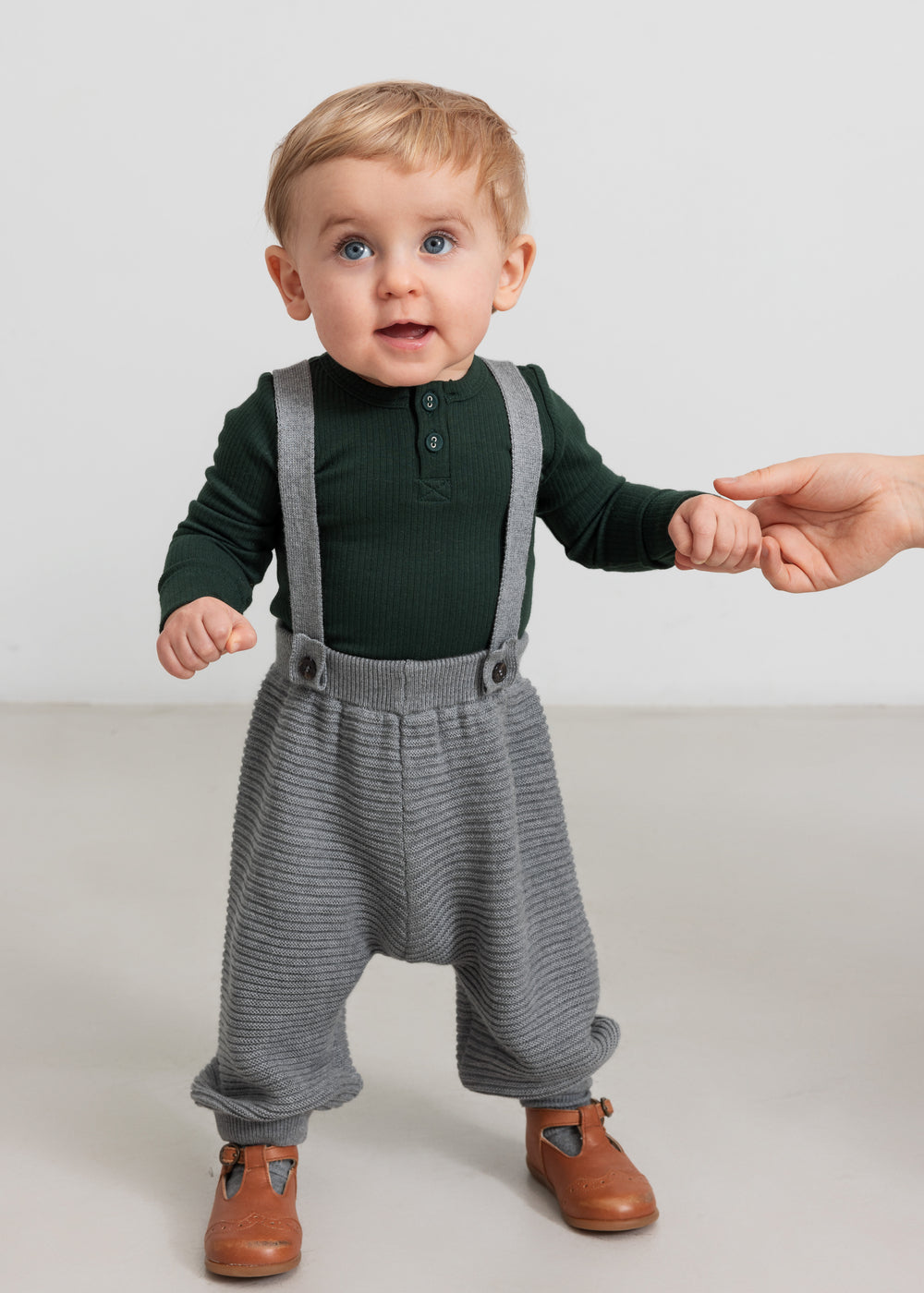 Baby iført grå strikkede selerbukser og mørkegrøn bluse
