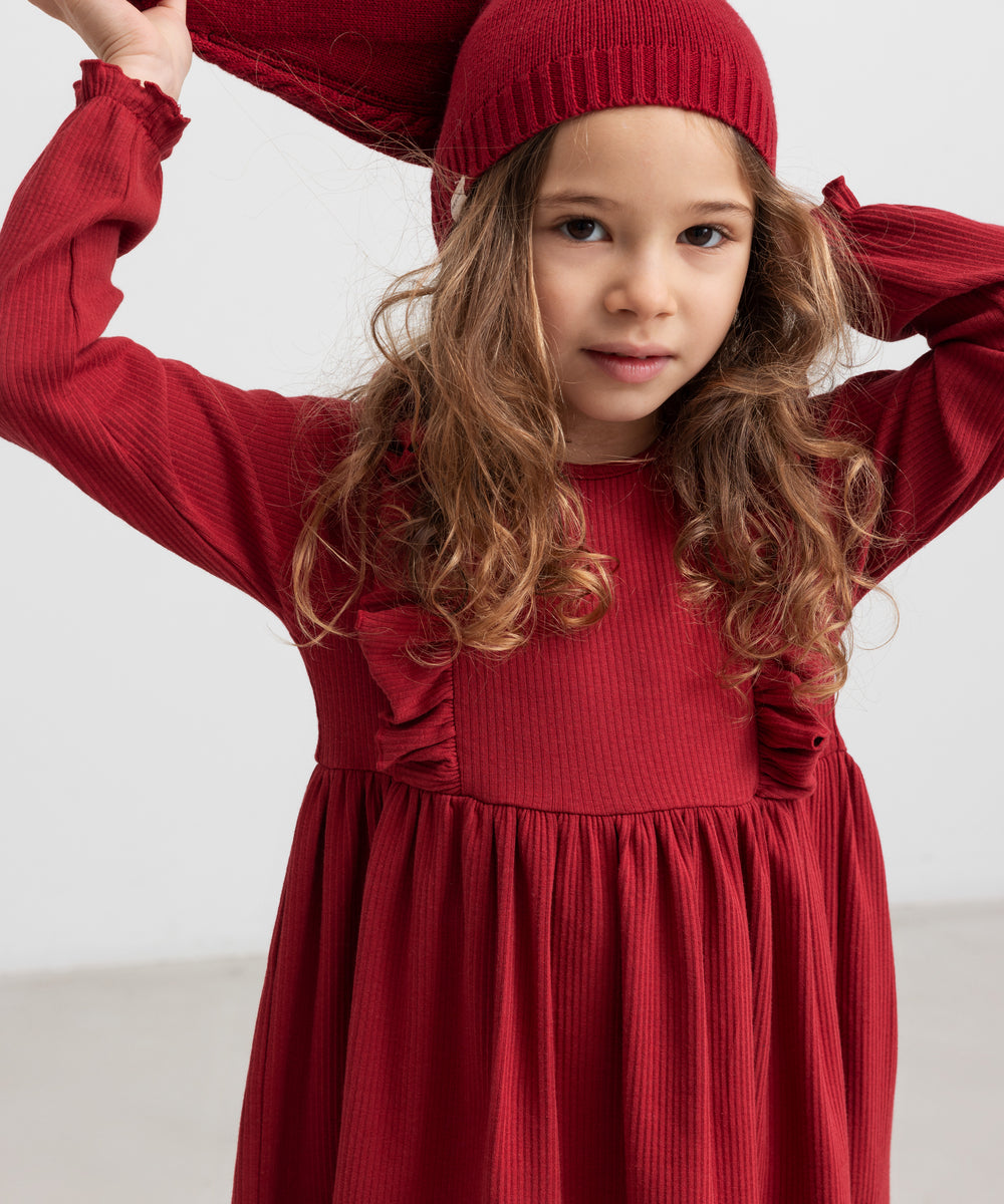 Pige i rød ribstrikket julekjole med flæser på skuldrene og nissehue
