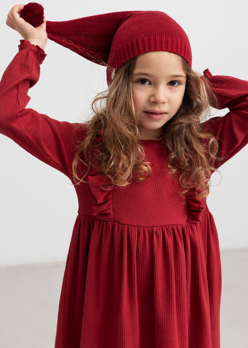 Pige i rød ribstrikket julekjole med flæser på skuldrene og nissehue