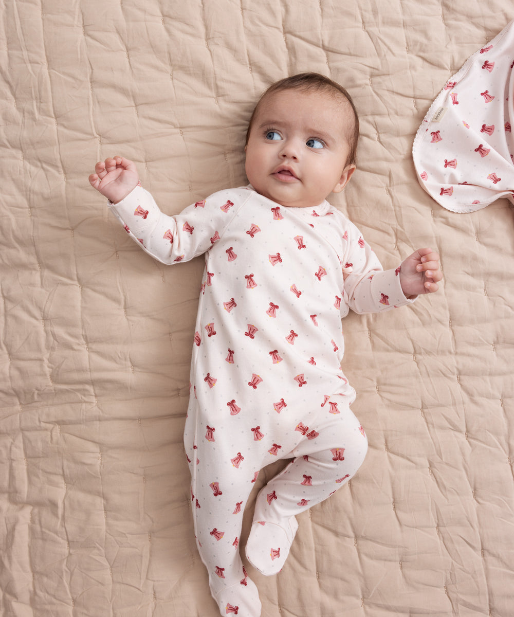 Baby iført cremefarvet heldragt med rødt juleklokkeprint liggende på tæppe