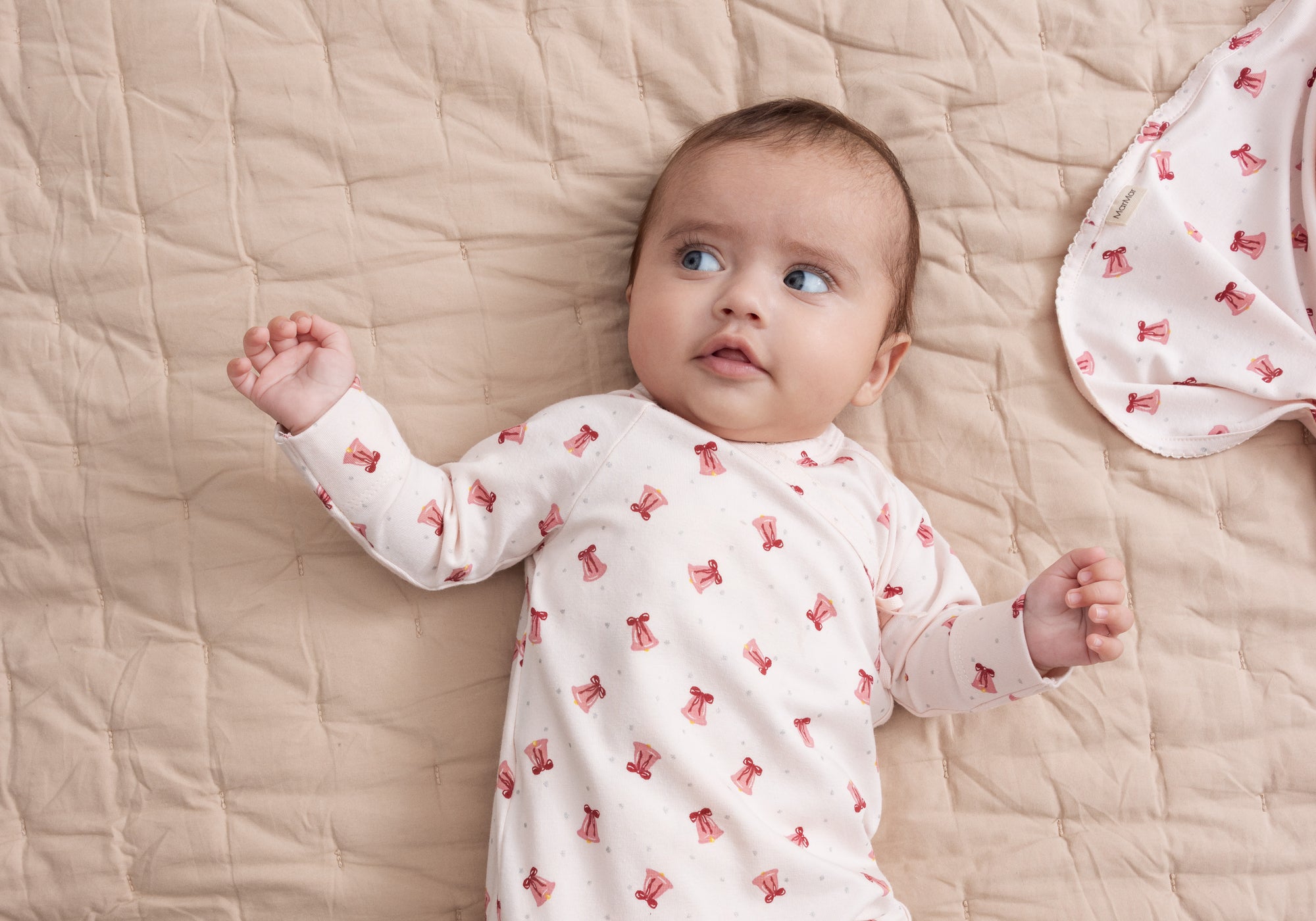 Nyfødt baby i hvid heldragt med håndtegnet print af små røde juleklokker