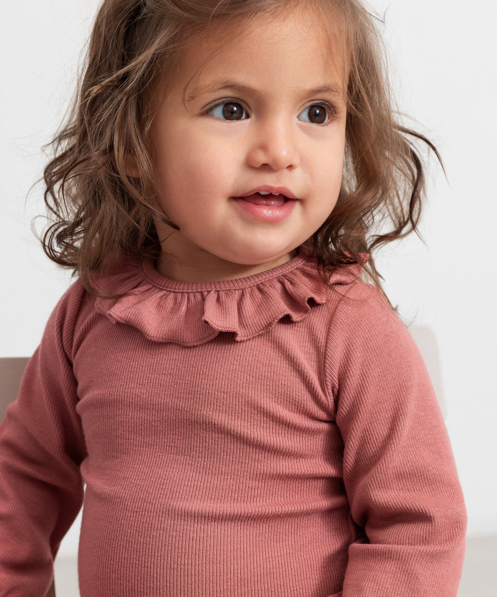 Baby iført støvet rosa body med flæsekrave