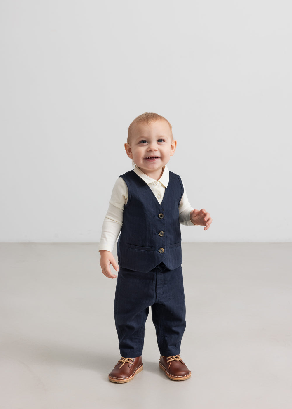 Baby iført mørkeblå vest, skjorte og bukser i festligt juletøj til baby