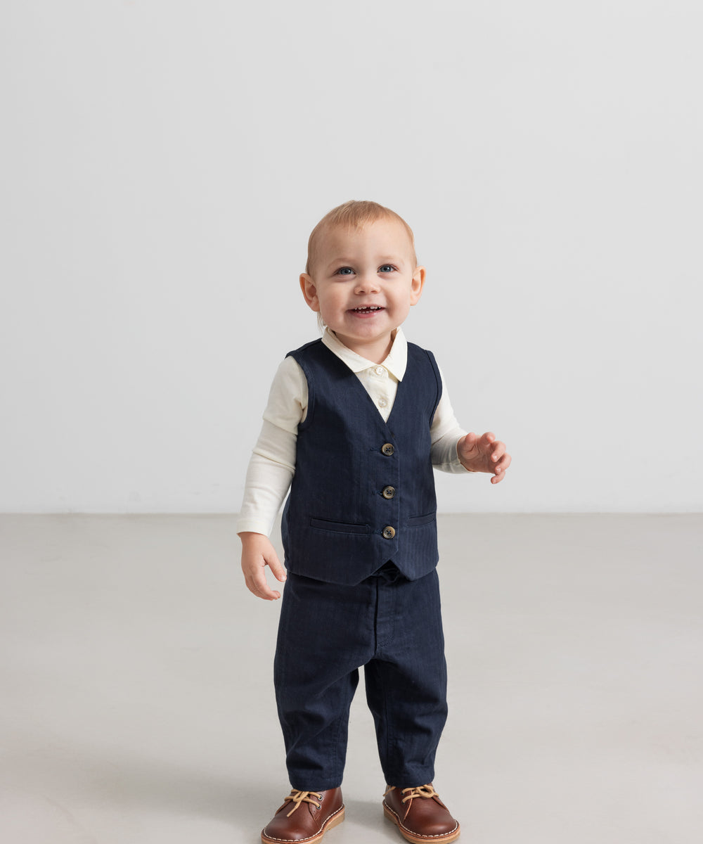 Baby iført mørkeblå vest, skjorte og bukser i festligt julesæt til baby