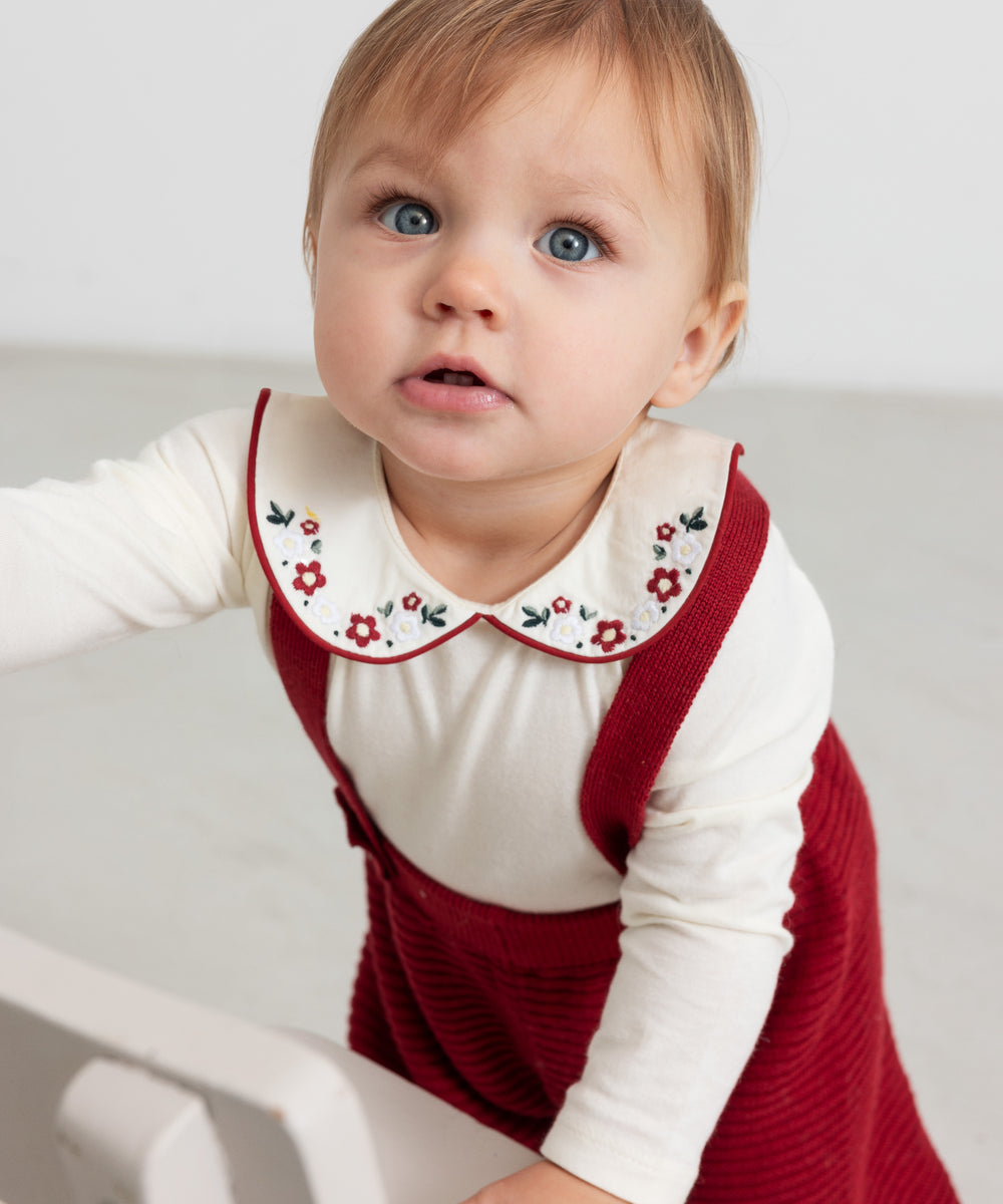 Baby iført hvid bodystocking med blomsterbroderet krave og julerød selekjole