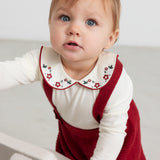 Baby iført røde strikkede selerbukser og hvid julebluse med krave og blomsterbroderier