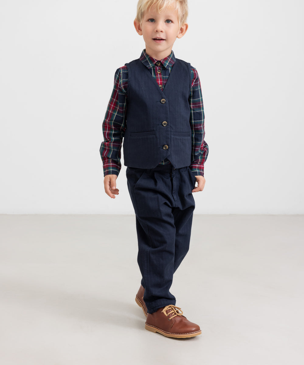 Dreng iført mørkeblå festbukser og vest med ternet skjorte i julelook til børn