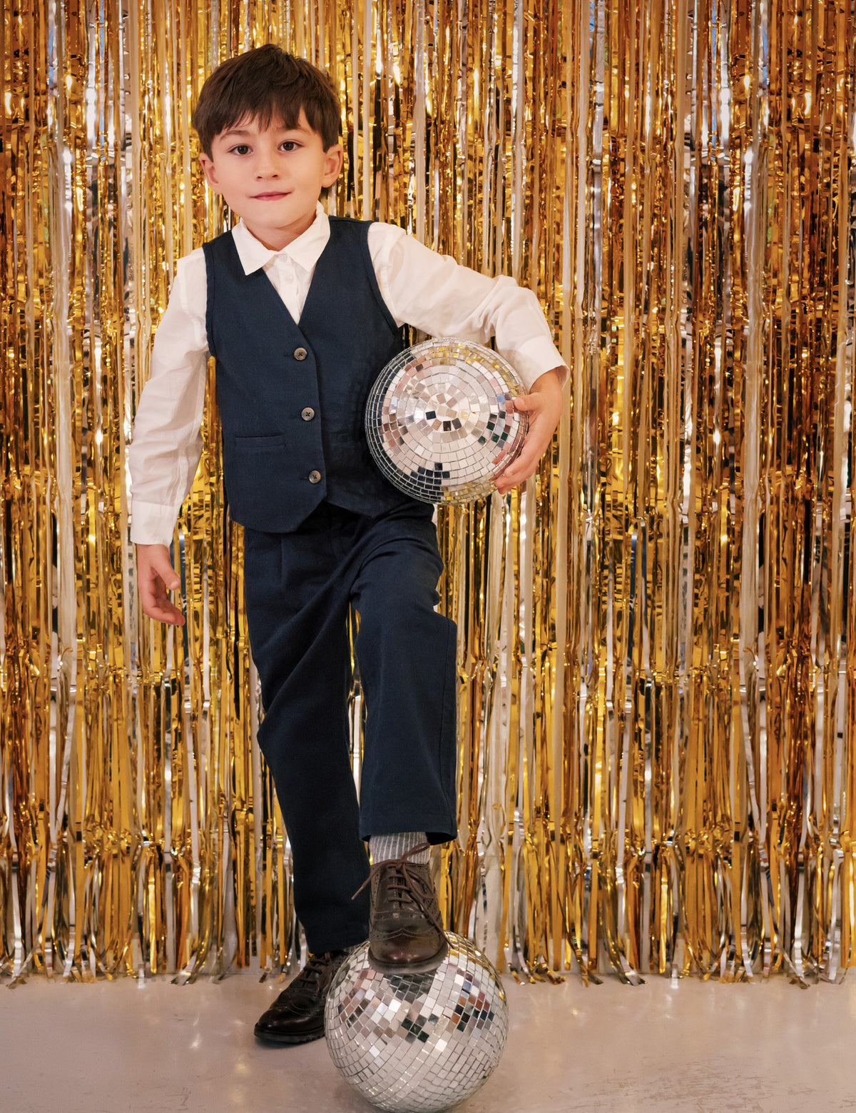 Dreng i festtøj med mørkeblåt jakkesæt og discokugle foran guldbaggrund