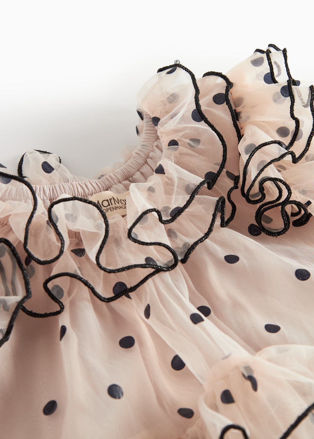 Nærbillede af lyserød tylkjole til børn med sorte prikker og bølgede flæsekanter