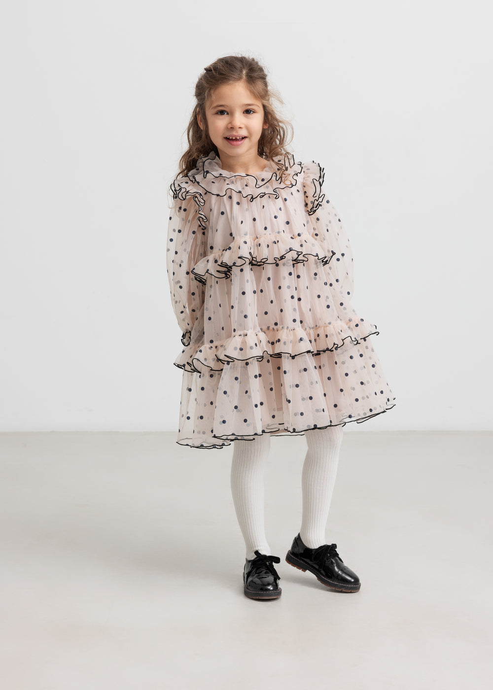 Pige iført lys beige julekjole i tyl med sorte prikker og hvide strømpebukser til børn