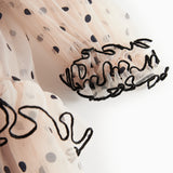 Nærbillede af ærme med sorte flæser og prikker på lys beige julekjole i tyl til børn