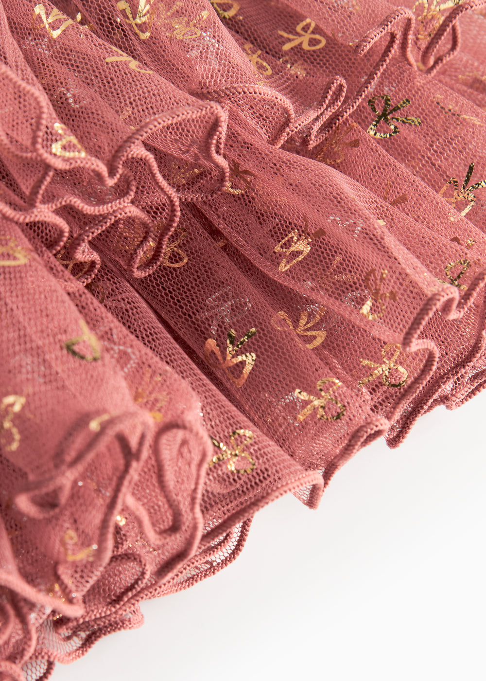 Detalje af tylstof på nederdel til børn med små gyldne prikker og flæser på rosa nederdel