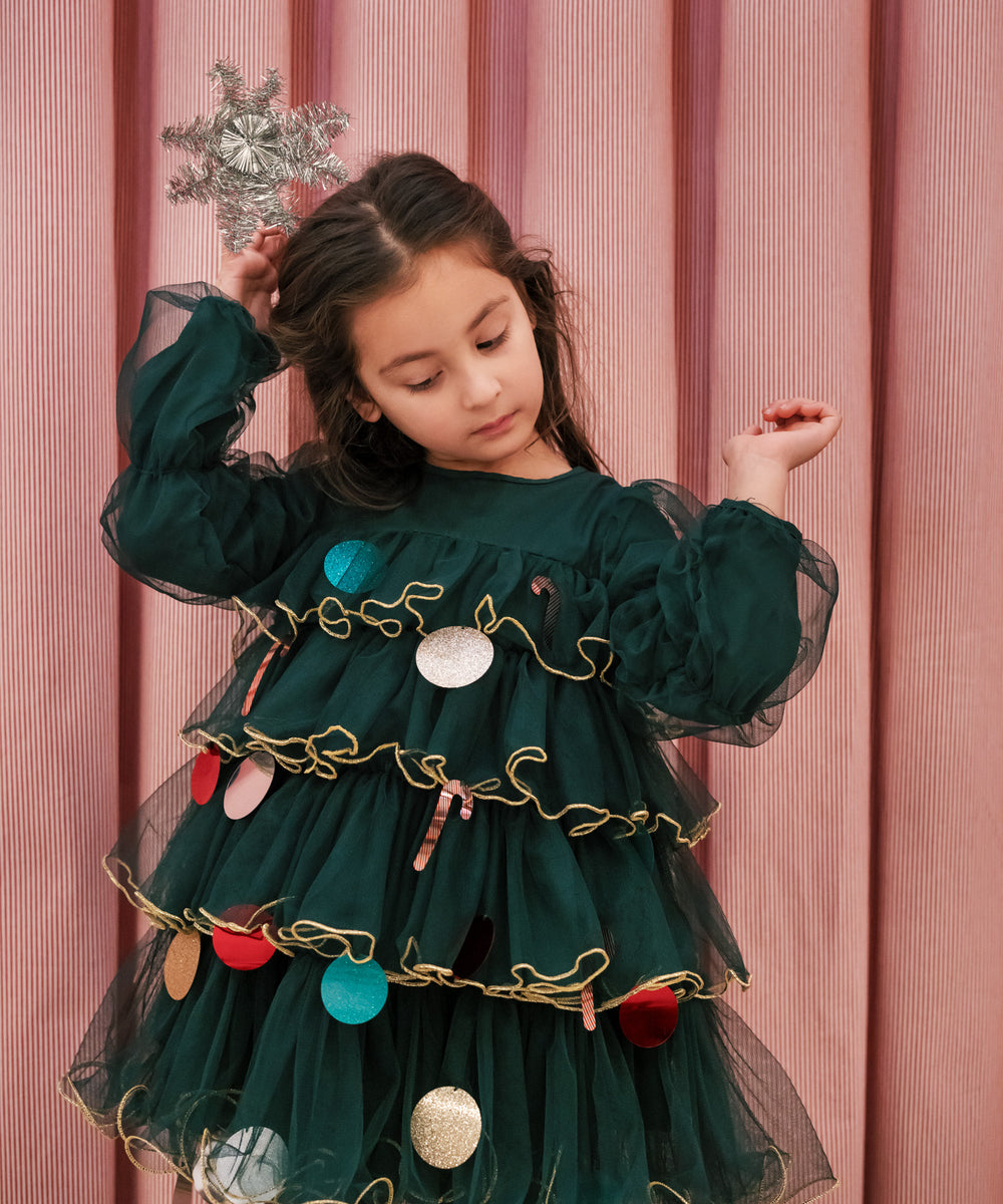 Pige iført mørkegrøn julekjole i tyl med guldkanter og juledetaljer til børn