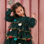 Pige iført mørkegrøn julekjole i tyl med guldkanter og juledetaljer til børn