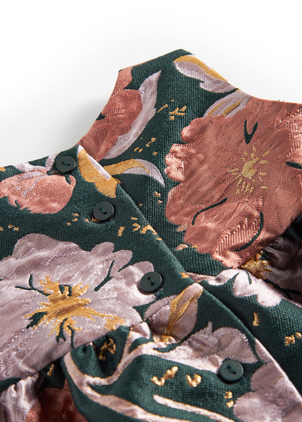 Nærbillede af mørkegrønt glansstof med blomsterprint og gyldne detaljer på festkjole til baby