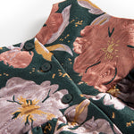 Nærbillede af mørkegrønt glansstof med blomsterprint og gyldne detaljer på festkjole til baby