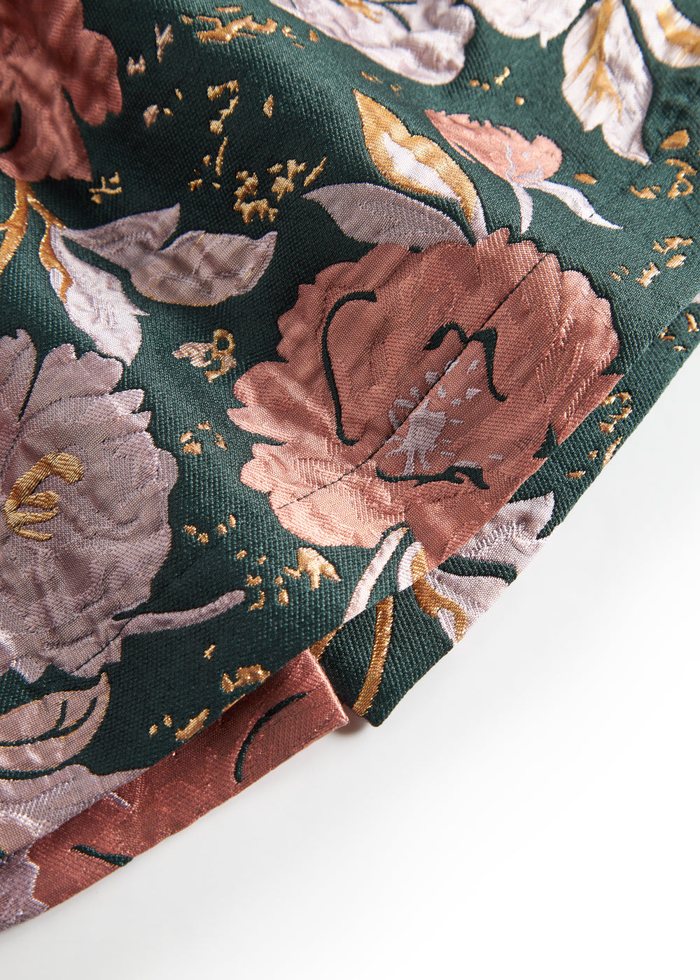 Nærbillede af mørkegrønt glansstof med blomsterprint og gyldne detaljer på festkjole til baby