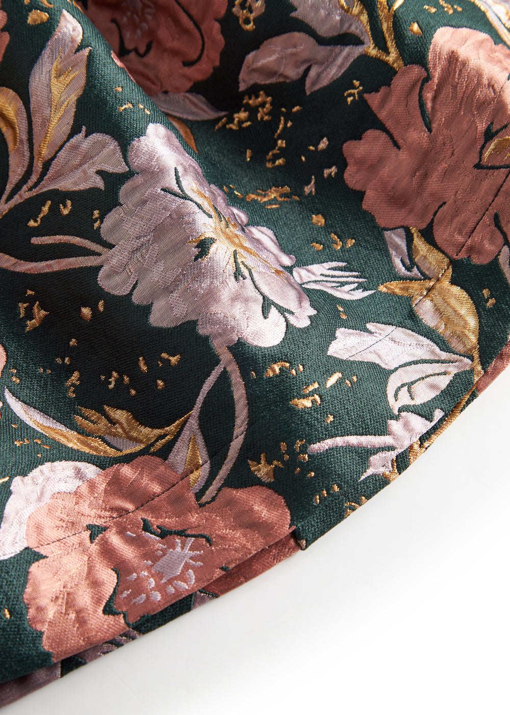 Nærbillede af mørkegrønt glansstof med blomsterprint og gyldne detaljer på festkjole til børn