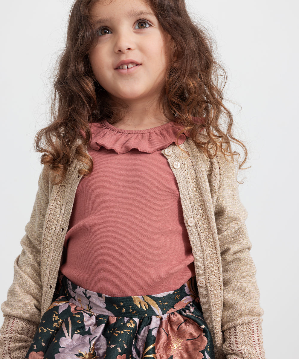 Pige iført mørkegrøn nederdel med blomsterprint, rosa bluse og beige cardigan til børn