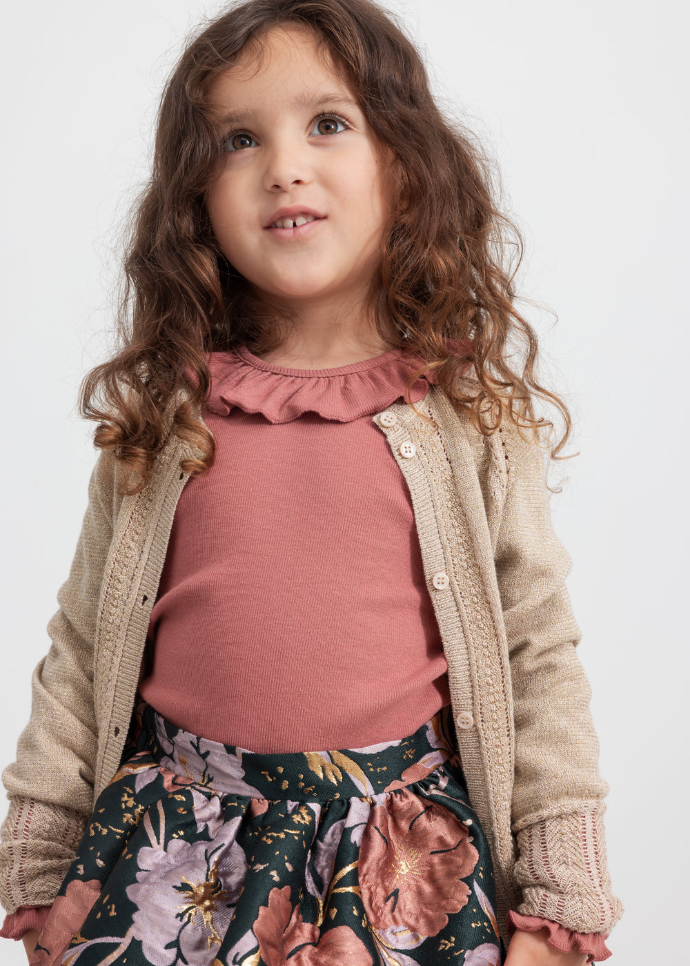 Pige iført mørkegrøn nederdel med blomsterprint, rosa bluse og beige cardigan til børn