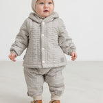 Baby iført brunstribet termo jakke og bukser med knapper samt beige strikket hue