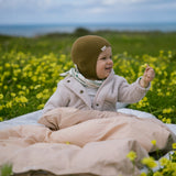 Baby iført brun strikket babyhjelm i udendørs miljø