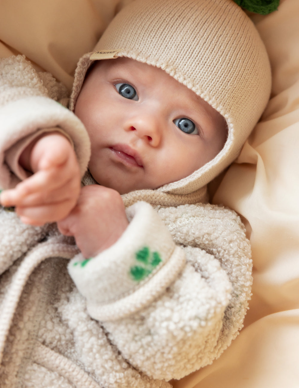 Baby i beige fleecejakke og beige strikket hue set tæt på