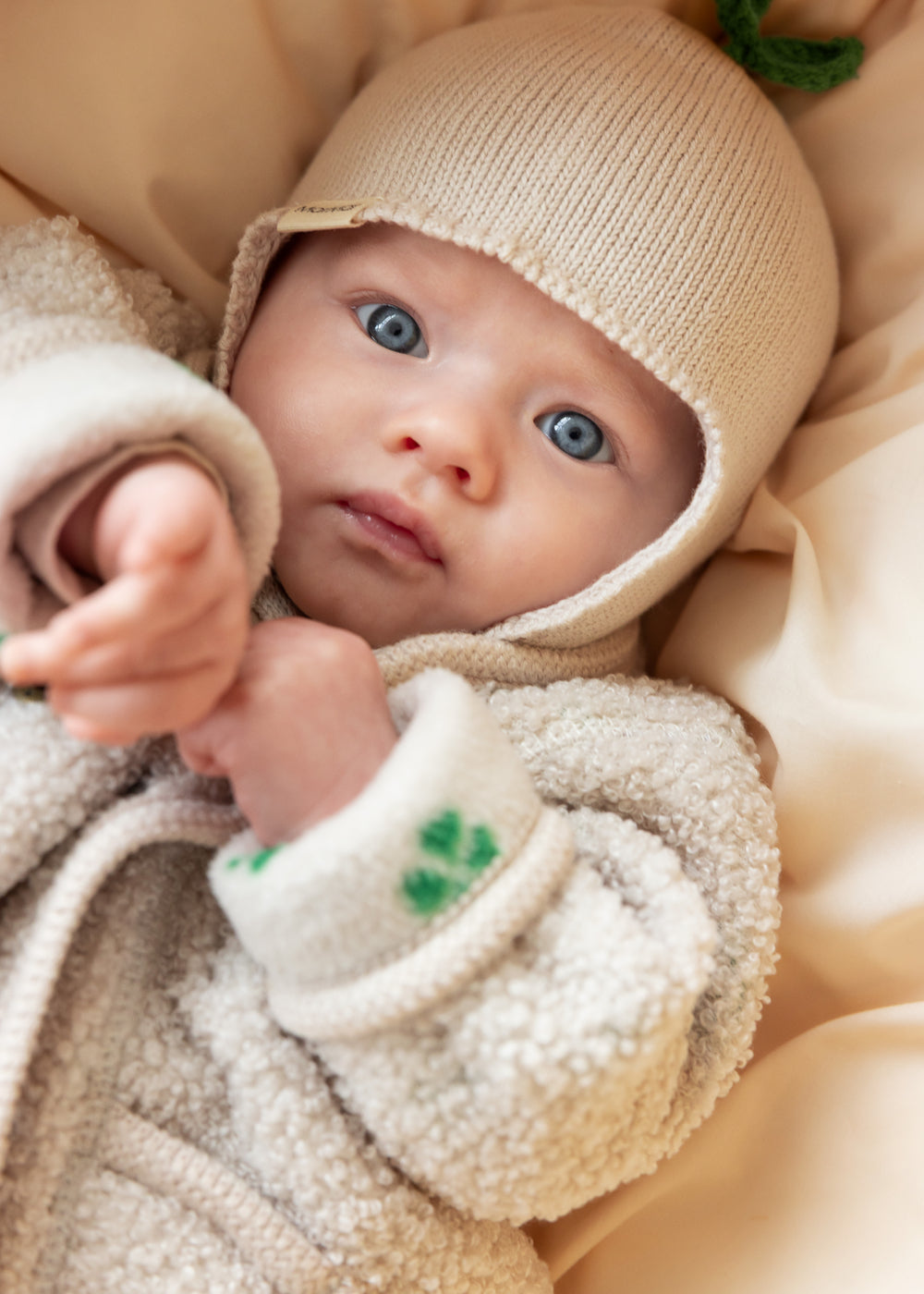 Baby i beige fleecejakke og beige strikket hue set tæt på