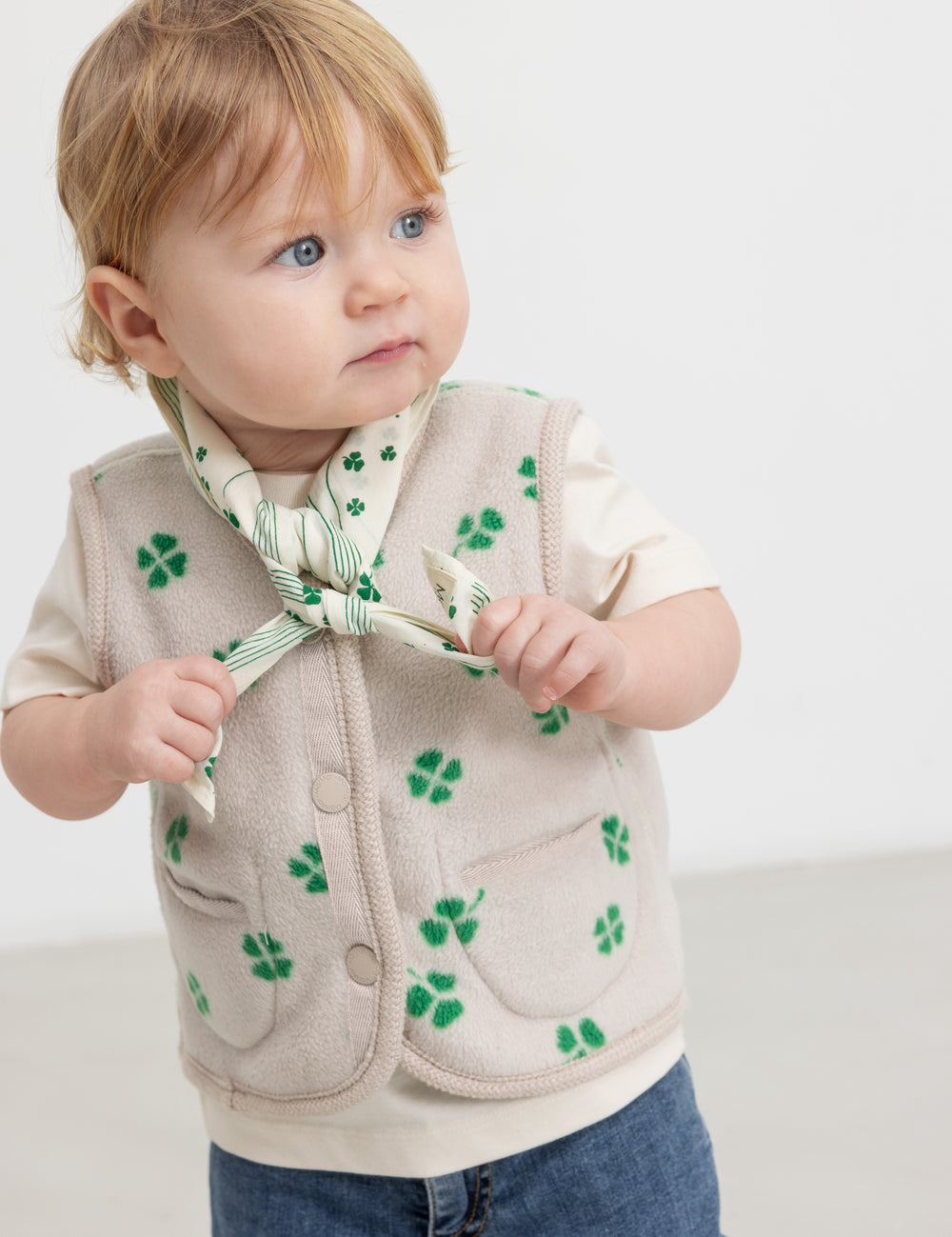 Baby iført beige vest med grønt kløverprint og knapper