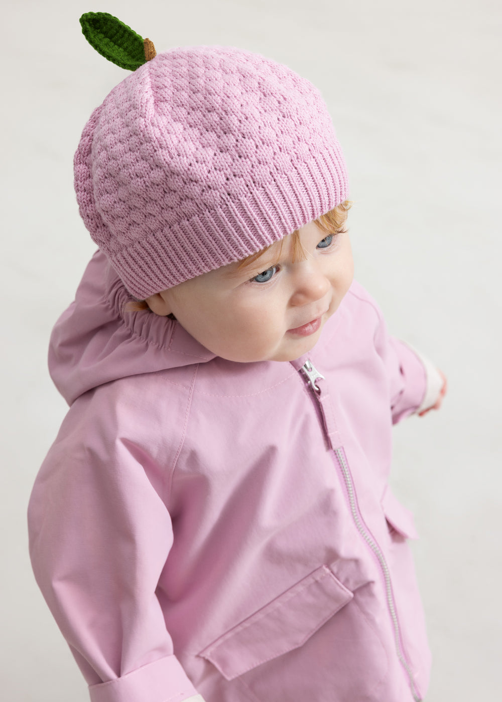 Baby i lyserød overgangsjakke og lyserød strikket hue