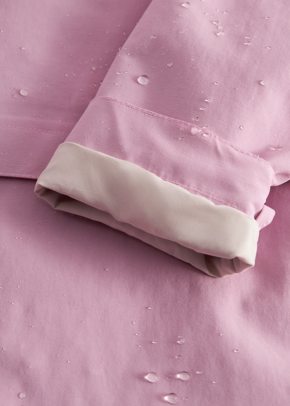 Detalje af lyserød overgangsjakke med vandperler på stof