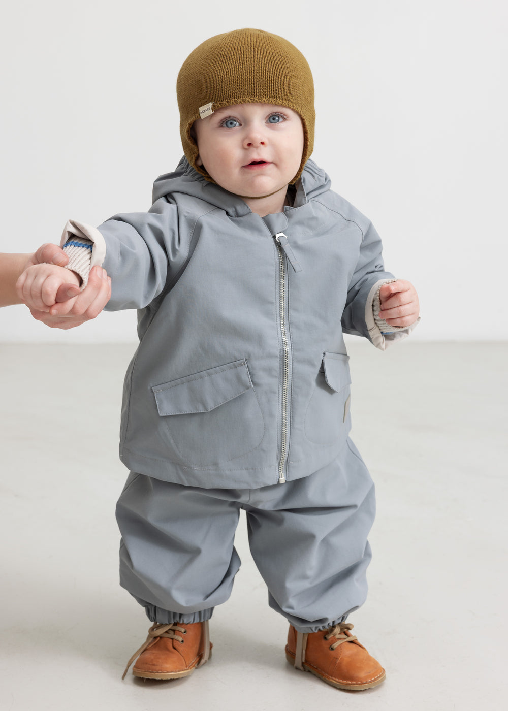 Baby iført grå overgangsjakke og grå overtræksbukser