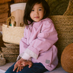 Barn iført lyserød overgangsjakke siddende på bænk