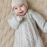 Baby iført brunstribet termodragt og beige hue liggende på tæppe