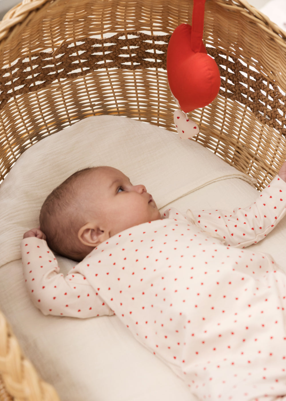 Baby liggende i kurv med rød musikuro over sig