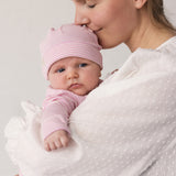 Baby iført lyserød hue holdt i favn af voksen